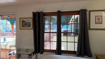 A hotel room with a bed, a window with curtains, a small table with chairs, and a view of the outside balcony.
