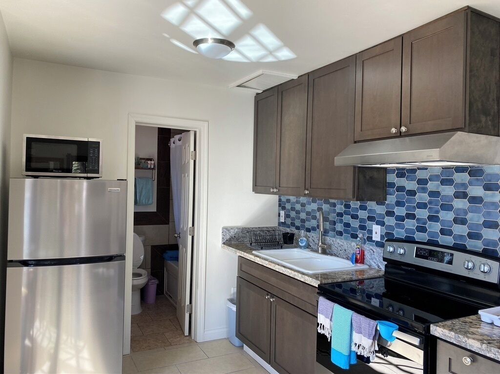 A modern kitchen with stainless steel appliances, dark wooden cabinets, a tiled backsplash, and a window providing natural light.