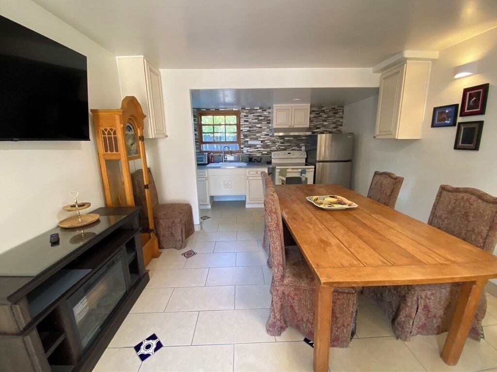A compact kitchen with white cabinets, a wooden dining table, and a TV mounted on the wall.