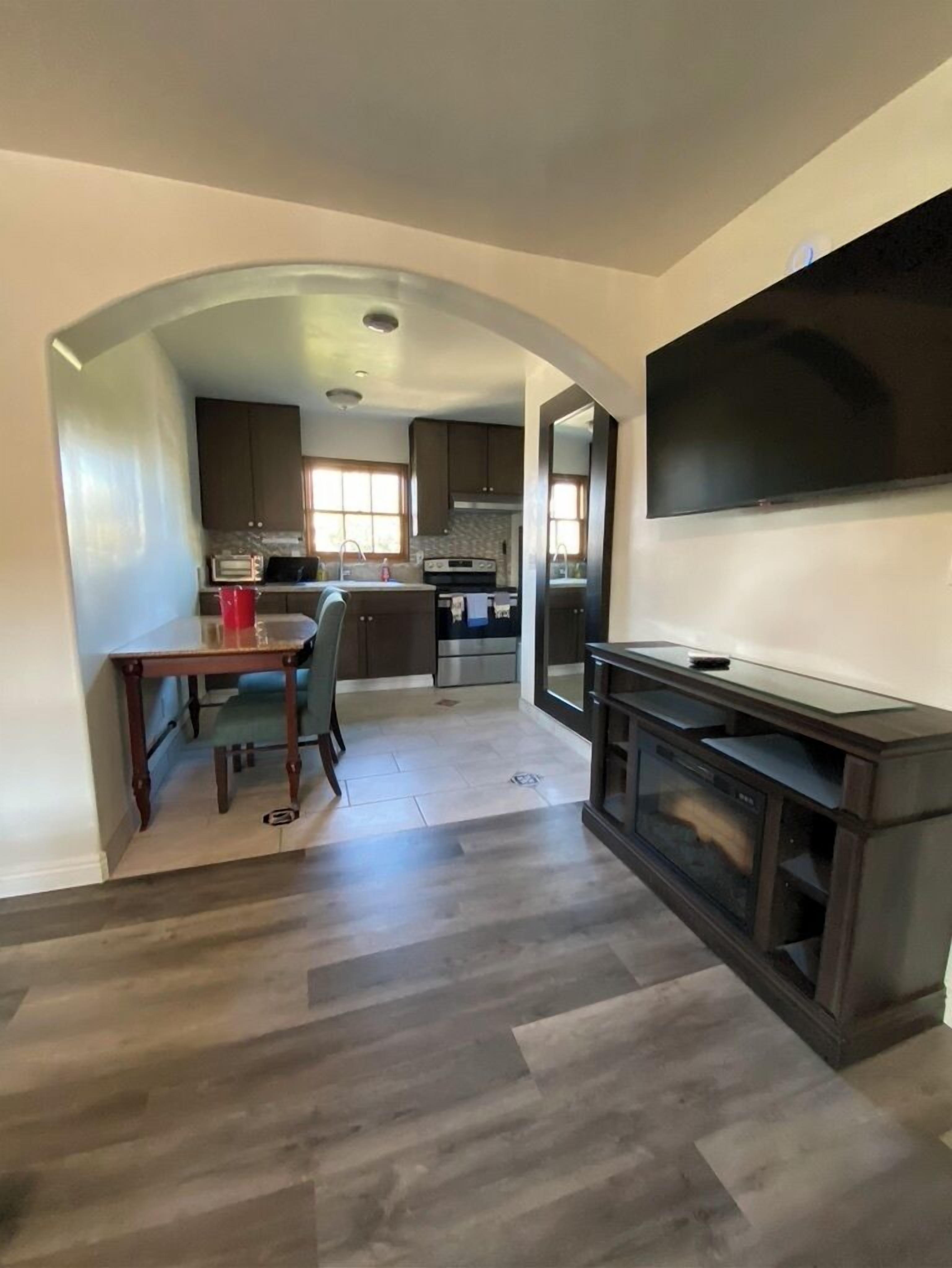 A modern kitchen with an island, a dining area with a table and chairs, and a large flat-screen TV mounted on the wall.