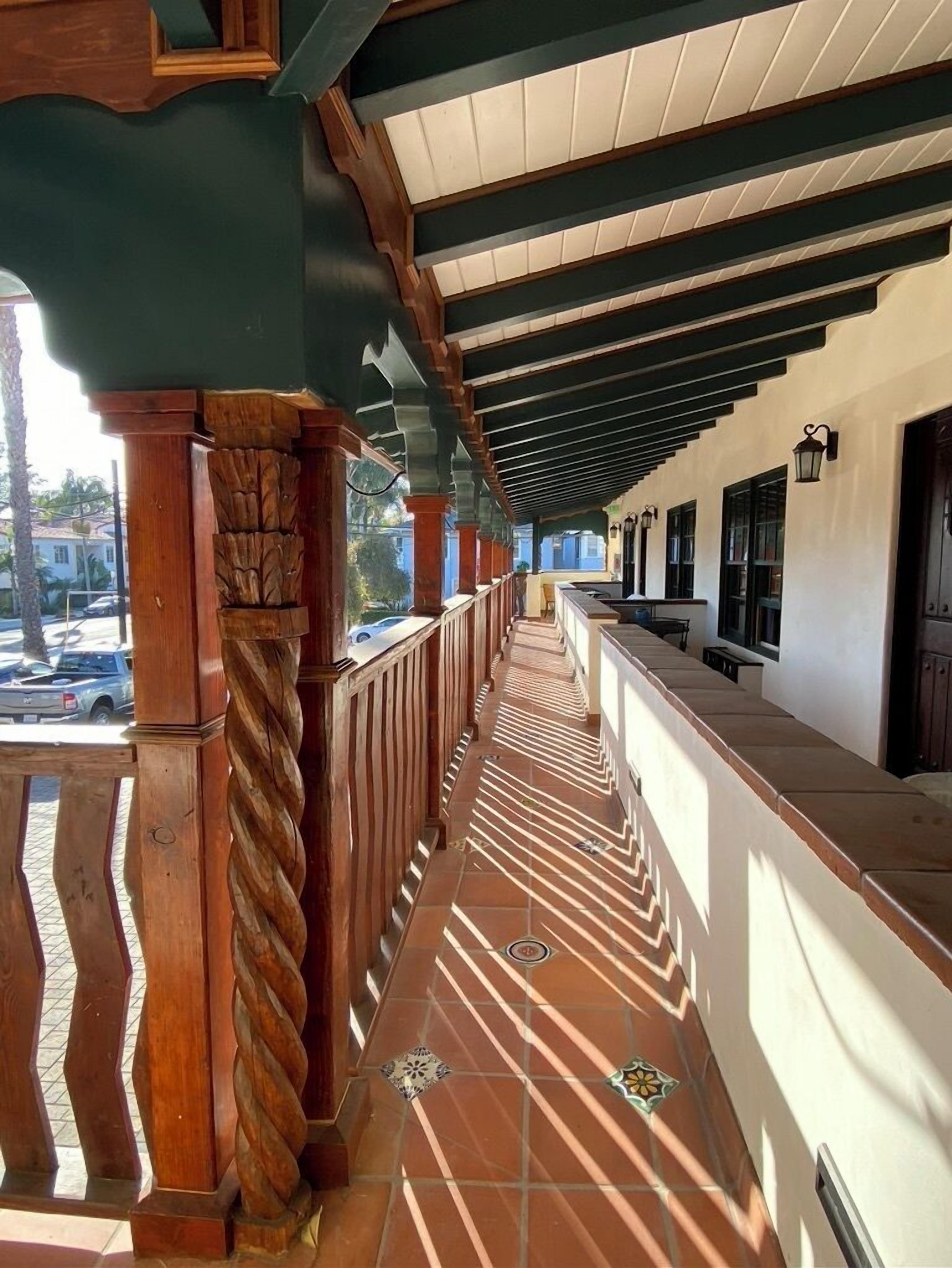 A covered outdoor area with a tiled floor, wooden railings, and a series of windows along the wall.
