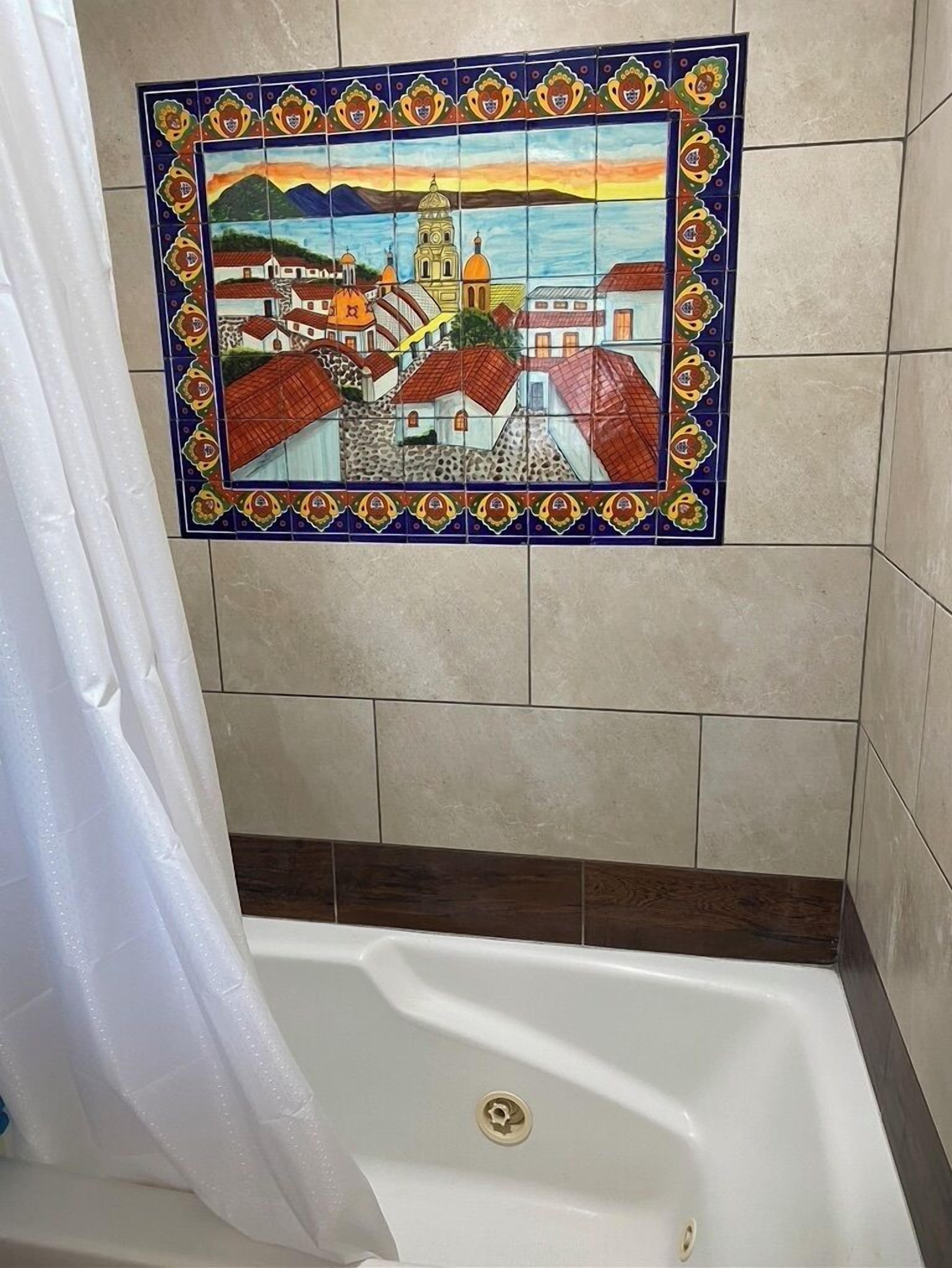 A bathroom with a tiled wall featuring a colorful mosaic of a town scene.