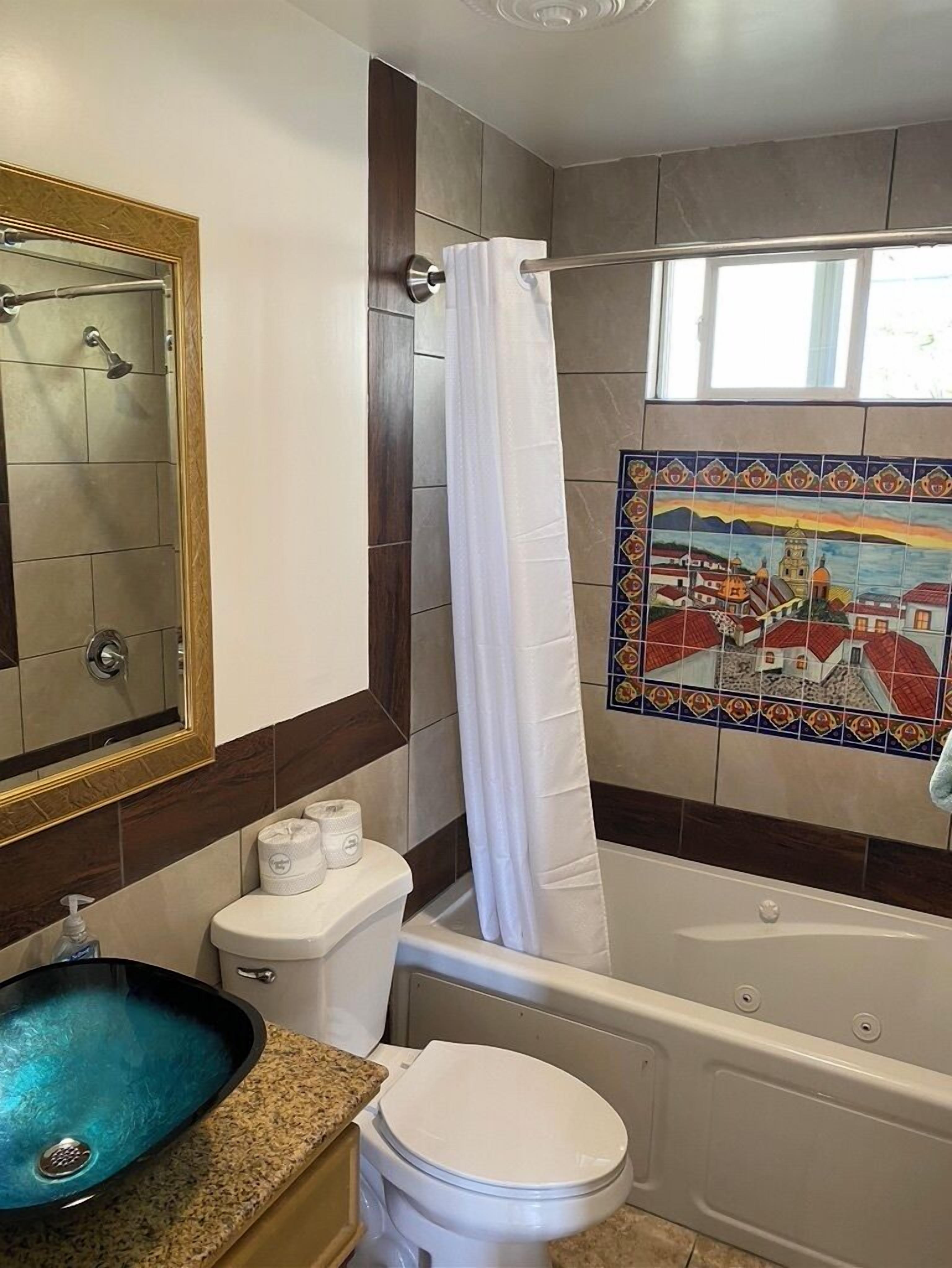 Een badkamer met een bad, toilet, wastafel met glazen kom en douche.