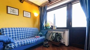 A room with a blue checkered sofa, a radiator, a window with curtains, and a small plant. - WONDERFUL APARTMENT IN RESIDENCE WITH A VIEW. (Sestriere)