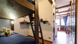 A bunk bed with a ladder, a small shelf with toys, and a window with curtains. - WONDERFUL APARTMENT IN RESIDENCE WITH A VIEW. (Sestriere)