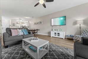 Una sala de estar moderna con un sofá gris, una mesa de centro blanca y un televisor montado en la pared.