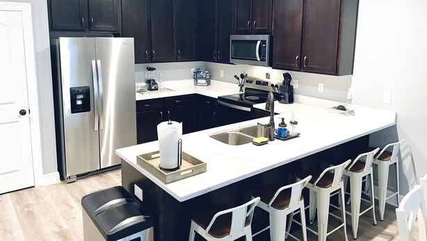 A modern kitchen with dark cabinets, stainless steel appliances, a central island with bar stools, and a white countertop. - Navarre+Beach, Pet Friendly + Kayak & paddle boards + BBQ grill.  (Navarre)