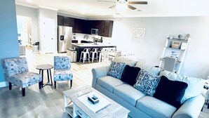 A living room with a sofa, two armchairs, a coffee table, and a dining area with a kitchen in the background. - Navarre+Beach, Pet Friendly + Kayak & paddle boards + BBQ grill.  (Navarre)