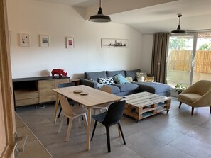 Un salon moderne comprenant un canapé, une table basse, une table à manger et des chaises. On peut y voir des tableaux encadrés au mur, une sculpture rouge sur le bureau et une fenêtre avec des rideaux.