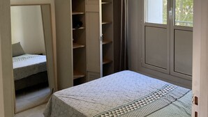 Un dormitorio con cama, armario, espejo y ventana.