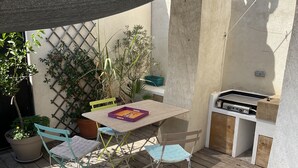 Un patio al aire libre con una mesa, sillas, una parrilla y plantas en macetas.