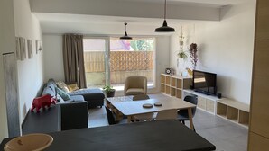 Un espacio de estar moderno con comedor, sofá, televisor y plantas.