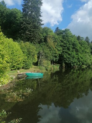 A calm river with dense greenery on both sides. A green boat is docked on the riverbank.