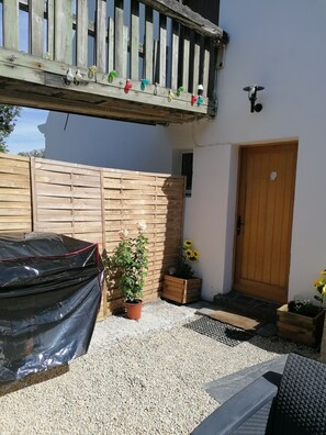 A covered car, a potted plant, a wooden fence, a door, and a small garden area with gravel.