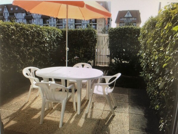 An outdoor patio with a round table and white chairs, surrounded by hedges. - Appartement RDJ 4 Pers, Jardinet, Piscine, Tennis (Cabourg)