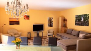 A living room with a glass-top dining table, a sofa, a TV, and a chandelier. - Ferienhaus in Idyllischer Dorfrandlage (Gülzow-Prüzen)