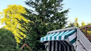 A wicker chair with a striped cushion, set against a backdrop of trees and a wooden fence. - Ferienhaus in Idyllischer Dorfrandlage (Gülzow-Prüzen)