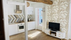 A compact kitchen with a microwave, oven, and modern appliances. There's a TV on a white cabinet, and a window with a view of the outside.