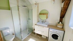 Een moderne badkamer met een glazen douchecabine, een wastafel met een houten aanrechtblad, een wasmachine en een spiegel met houten lijst.