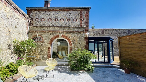 A stone building with a tiled patio, outdoor seating, and a glass door leading inside.