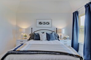 A neatly made bed with a striped blanket, two bedside tables with lamps, a framed picture above the bed, and a window with curtains. - New home, Argyle TX, 4 Bd rooms, 5 bds, 3 Bathrooms, Office, Gameroom, Sleeps 11 (Argyle)