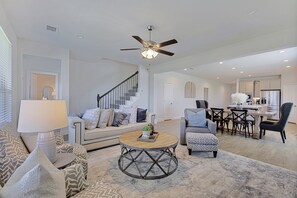 A spacious living room with a modern ceiling fan, a staircase, a dining area, and a kitchen. - New home, Argyle TX, 4 Bd rooms, 5 bds, 3 Bathrooms, Office, Gameroom, Sleeps 11 (Argyle)