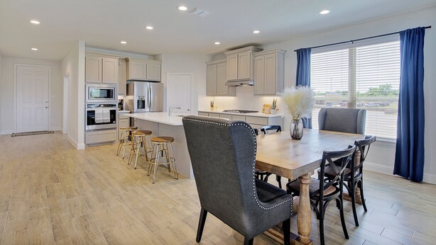 A modern kitchen with white cabinets, stainless steel appliances, and a wooden dining table with four chairs. - New home, Argyle TX, 4 Bd rooms, 5 bds, 3 Bathrooms, Office, Gameroom, Sleeps 11 (Argyle)