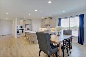 A modern kitchen with white cabinets, stainless steel appliances, and a wooden dining table with four chairs. - New home, Argyle TX, 4 Bd rooms, 5 bds, 3 Bathrooms, Office, Gameroom, Sleeps 11 (Argyle)