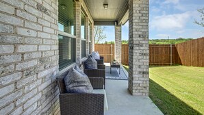 A covered patio with wicker furniture, a concrete floor, and a view of a wooden fence and lawn. - New home, Argyle TX, 4 Bd rooms, 5 bds, 3 Bathrooms, Office, Gameroom, Sleeps 11 (Argyle)