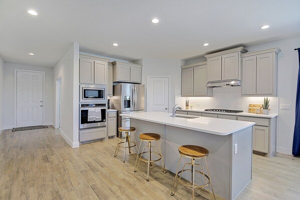 A modern kitchen with white cabinets, stainless steel appliances, and a central island with stools. - New home, Argyle TX, 4 Bd rooms, 5 bds, 3 Bathrooms, Office, Gameroom, Sleeps 11 (Argyle)