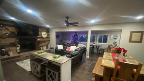 Eine moderne Küche mit einer zentralen Kochinsel, einem Essbereich mit Holztisch und -stühlen, einem schwarzen Ledersofa und einem Weihnachtsbaum.