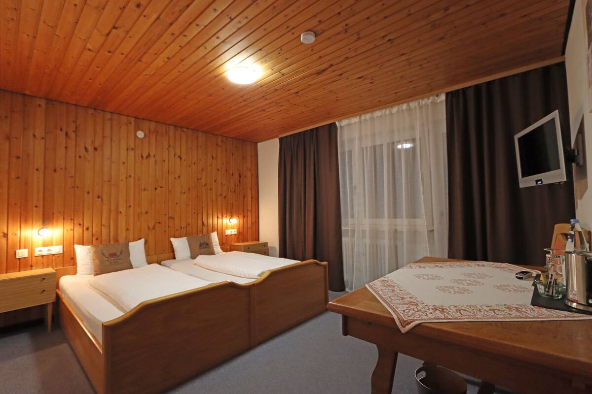 Une chambre aux murs lambrissés, équipée d’un lit double, de tables de chevet, d’un bureau et d’un téléviseur.