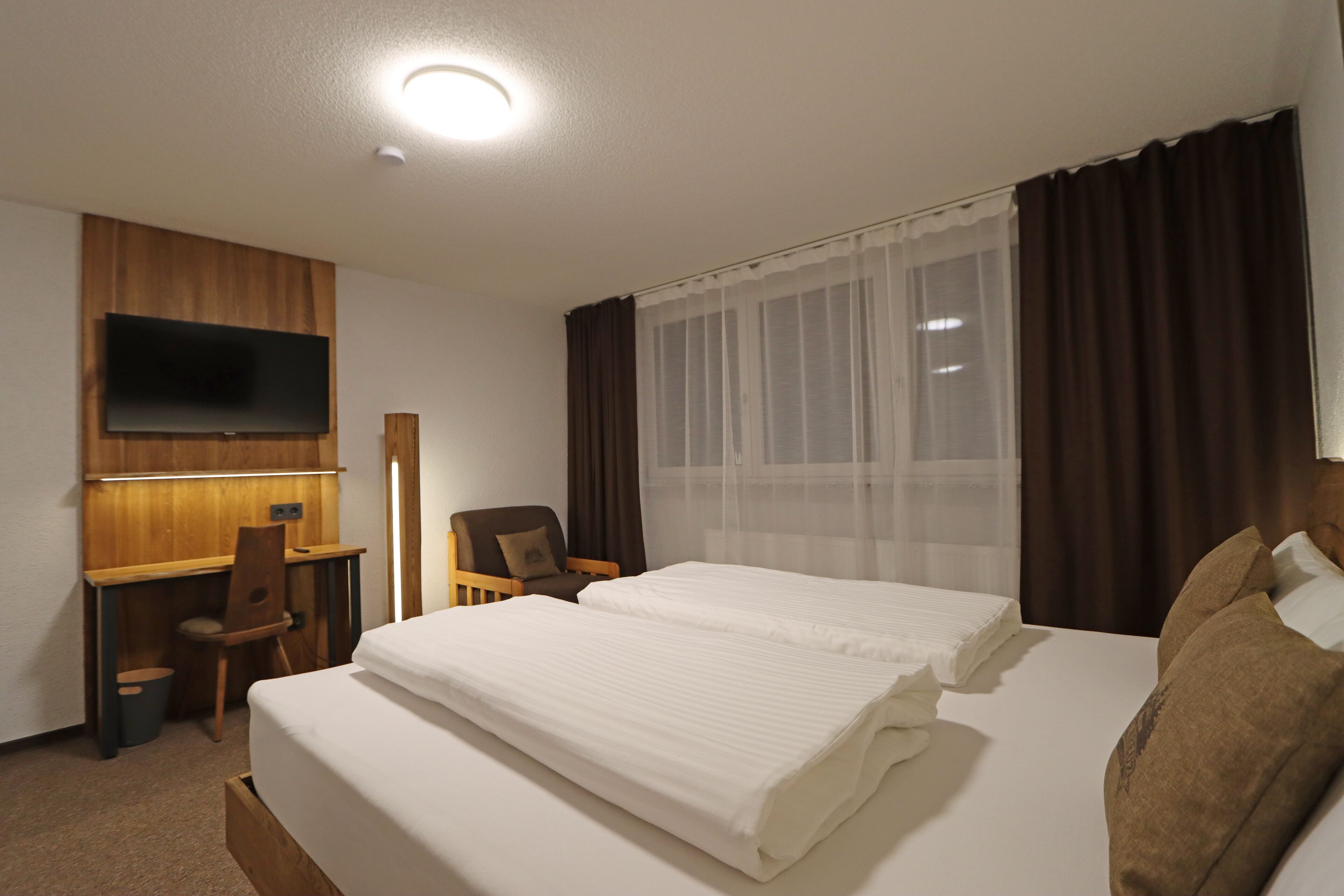 Habitación de hotel con cama, escritorio, silla, televisor y ventana con cortinas.