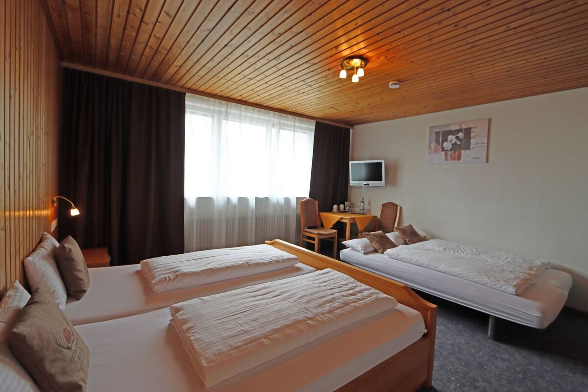 Une chambre d’hôtel avec deux lits, un bureau, une chaise, une télévision et une fenêtre avec des rideaux.