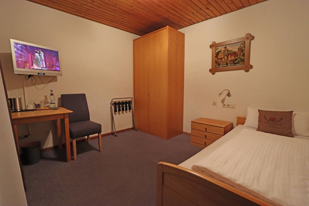 Une chambre à coucher comprenant un lit, un bureau avec une chaise, une armoire, un radiateur et un téléviseur fixé au mur.