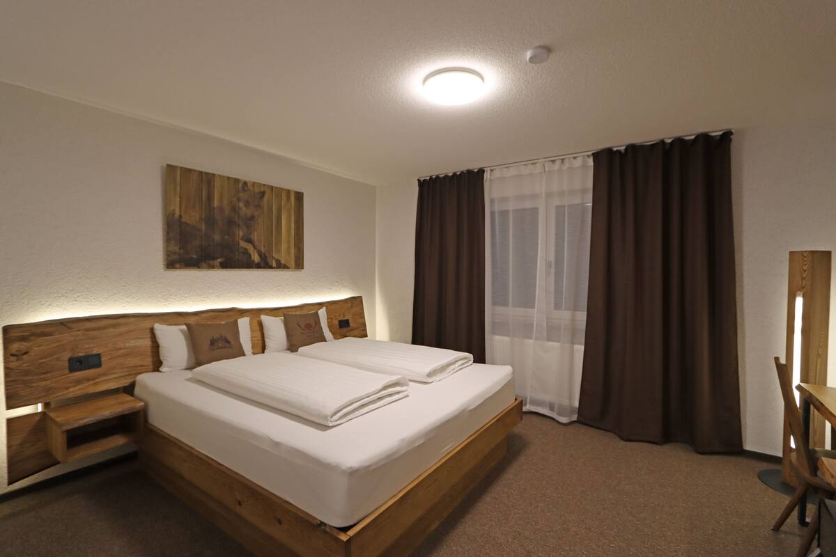 Une chambre d’hôtel avec un lit en bois, une table de chevet, une œuvre d’art accrochée au mur et une fenêtre avec des rideaux.