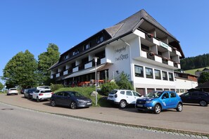 Een hotel met meerdere verdiepingen, balkons, een parkeerplaats en een helderblauwe lucht.