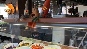 A buffet with various food items in bowls, a decorative gnome, and a rooster on the wall. - Hotel Kreuz Höhengasthof (Breitnau)