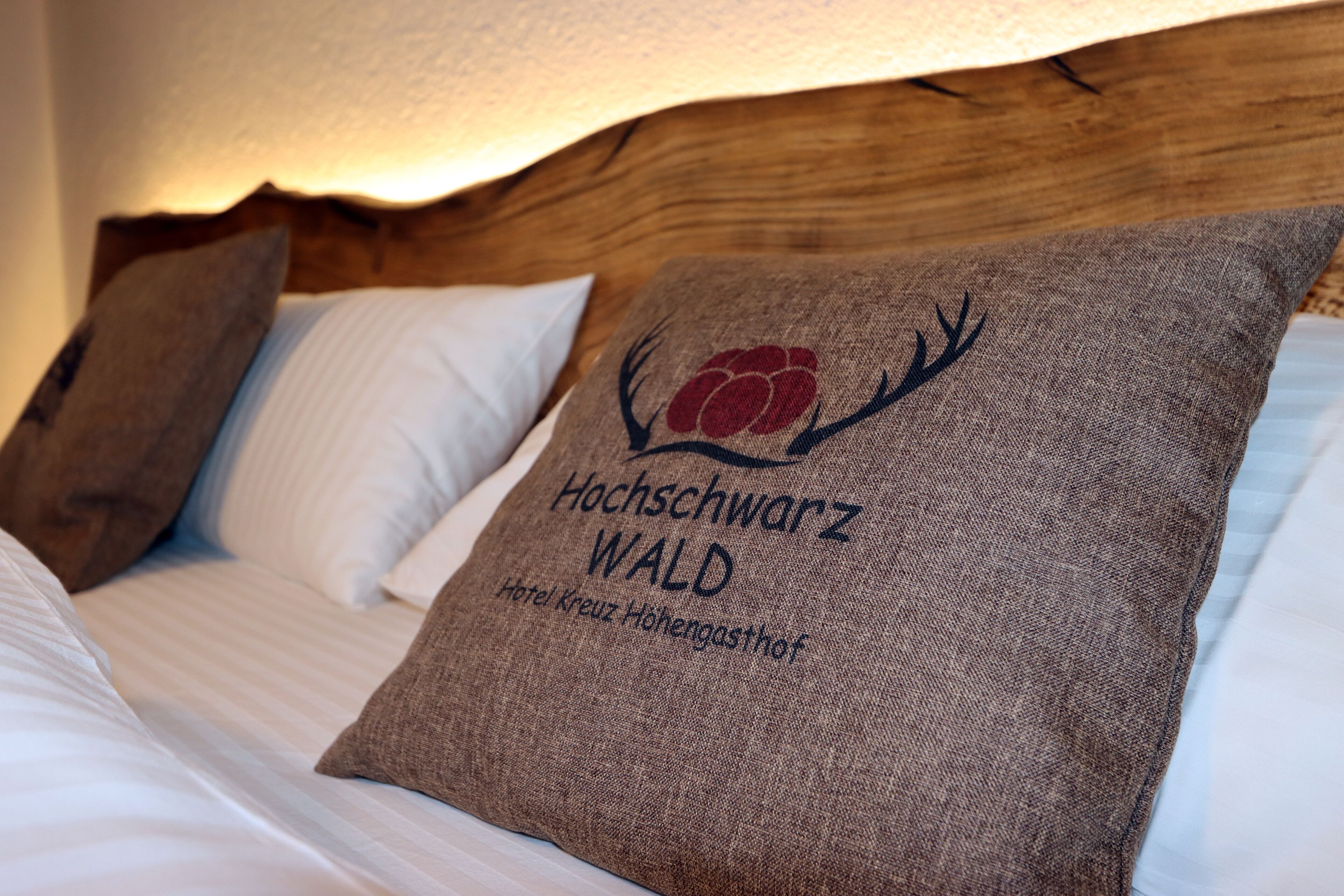 A bed with a pillow featuring a logo and text, a wooden headboard, and a textured wall.