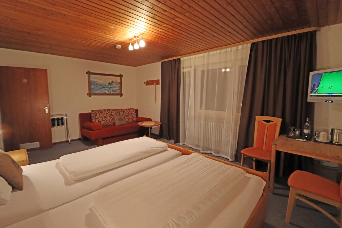 Une chambre d’hôtel avec deux lits, un canapé, une télévision et un plafond en bois.