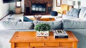 A living room with a brick fireplace, a ceiling fan, a flat-screen TV, a sofa, and a coffee table.