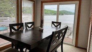 A dining area with a table and chairs, large windows with blinds, and a view of a lake and hills.