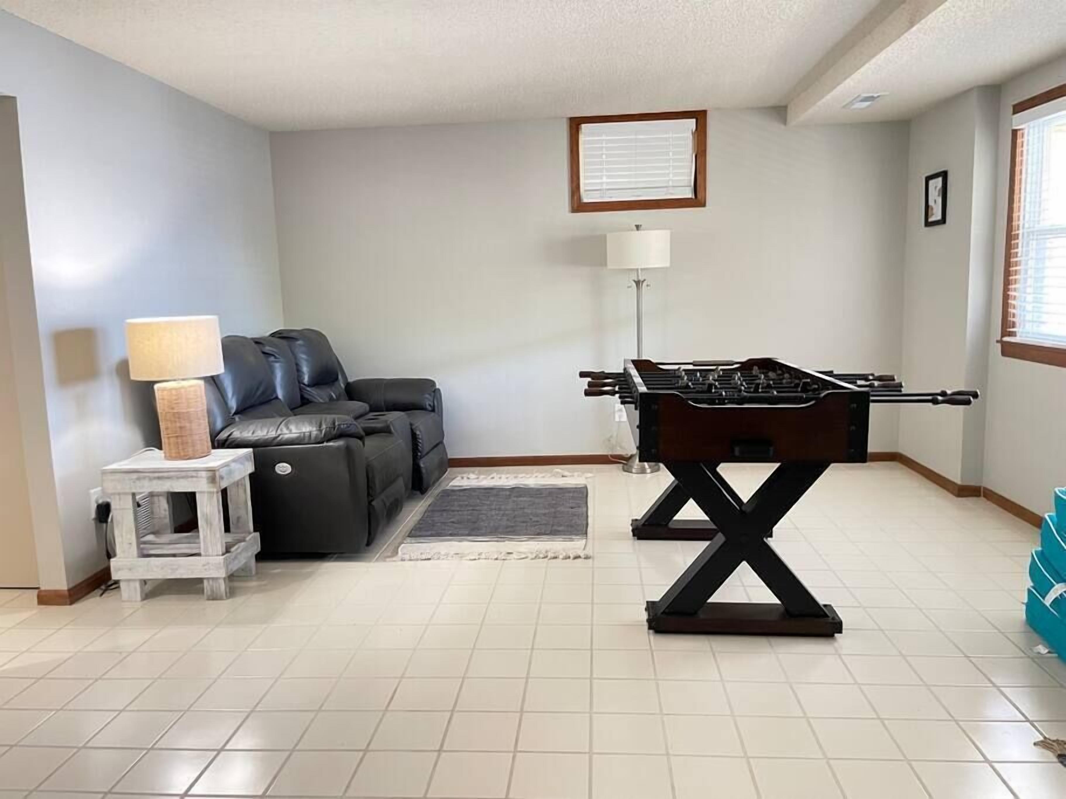 A living room with a sofa, a lamp, a foosball table, and a small side table.