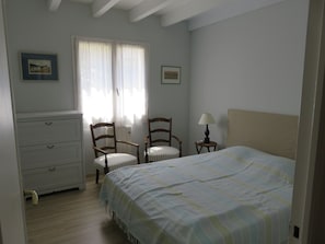 A bedroom with a bed, two chairs, a dresser, a lamp, and a window with curtains.