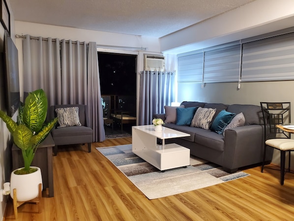 Una sala moderna con un sofá gris, una mesa de centro blanca y una planta grande.
