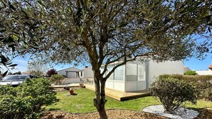 Une maison moderne avec un arbre dans le jardin avant, un petit potager et une voiture garée à proximité.