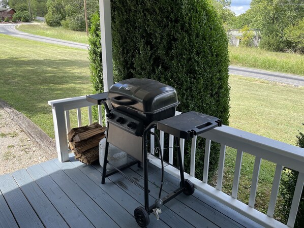 Een barbecue op een houten terras met een witte reling, omringd door groen.