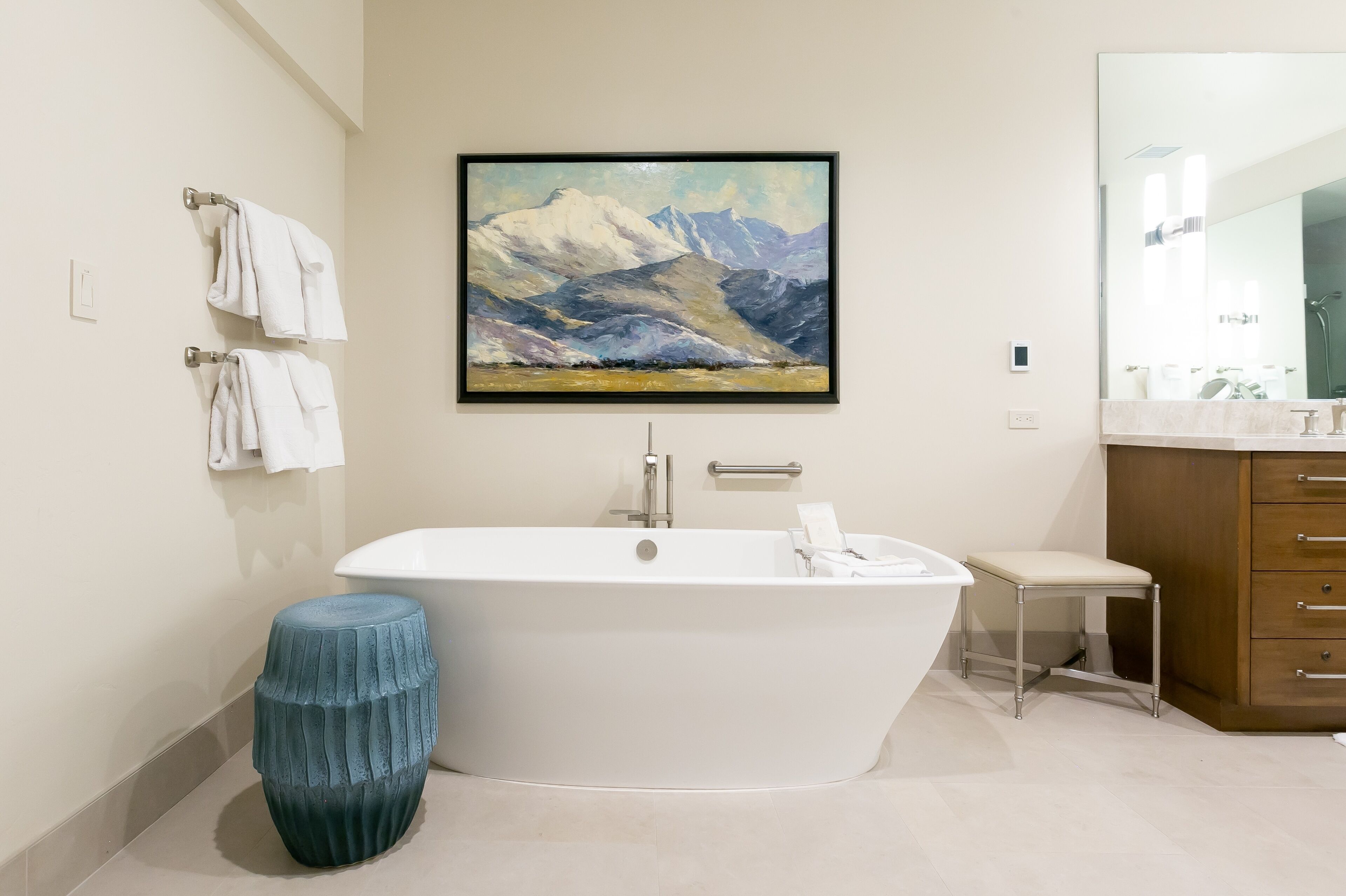 Un bagno moderno con una vasca freestanding, un mobile bagno in legno con specchio e un dipinto di montagne al muro.
