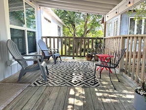 Una terraza techada con piso de madera, un tapete estampado y mobiliario exterior que incluye sillas y una mesa.