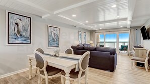 A spacious living area with a dining table and chairs, a dark sofa, and a flat-screen TV. - Fully Renovated oceanfront getaway with a modern coastal feel and amazing ocean views! (Fernandina Beach)